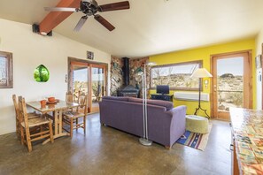 A living room with a sofa, dining table, chairs, a ceiling fan, and a view through a window.