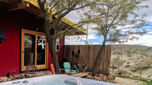A hot tub area with a wooden deck, a red building, and a view of the desert landscape.