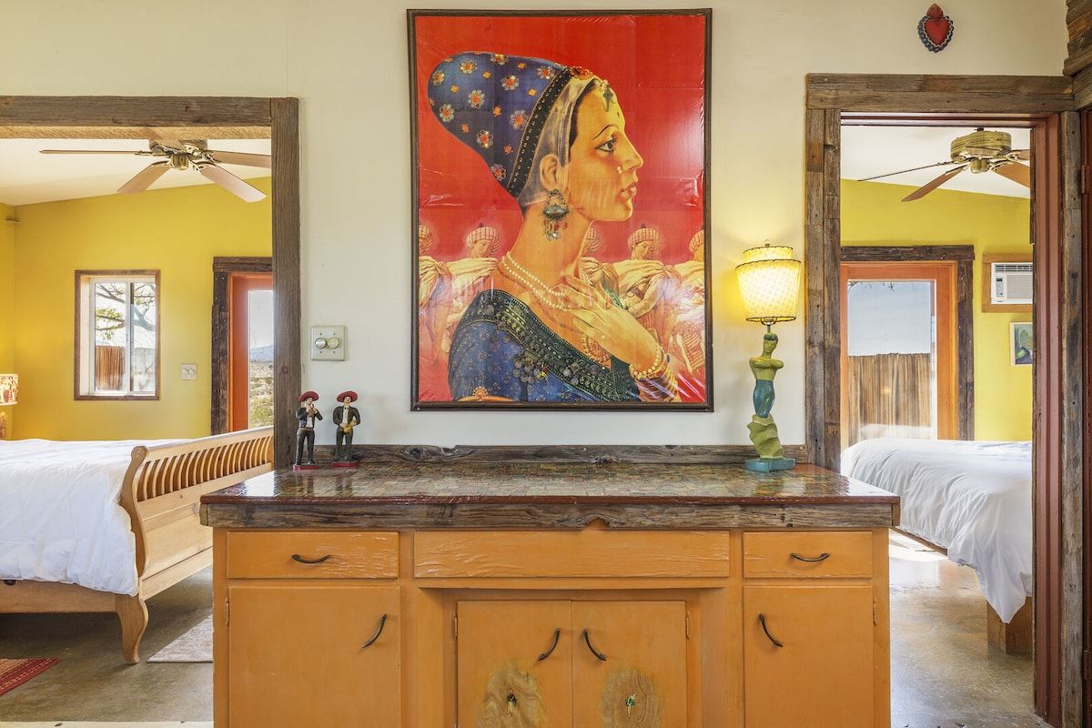 Une chambre d’hôtel avec un lit, une commode en bois, un tableau et un ventilateur de plafond.