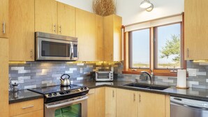 A modern kitchen with wooden cabinets, a stainless steel microwave, a built-in oven, a toaster, and a dishwasher. - MoonView Modern | Hot tub, BBQ & Private Pool! (Joshua Tree)