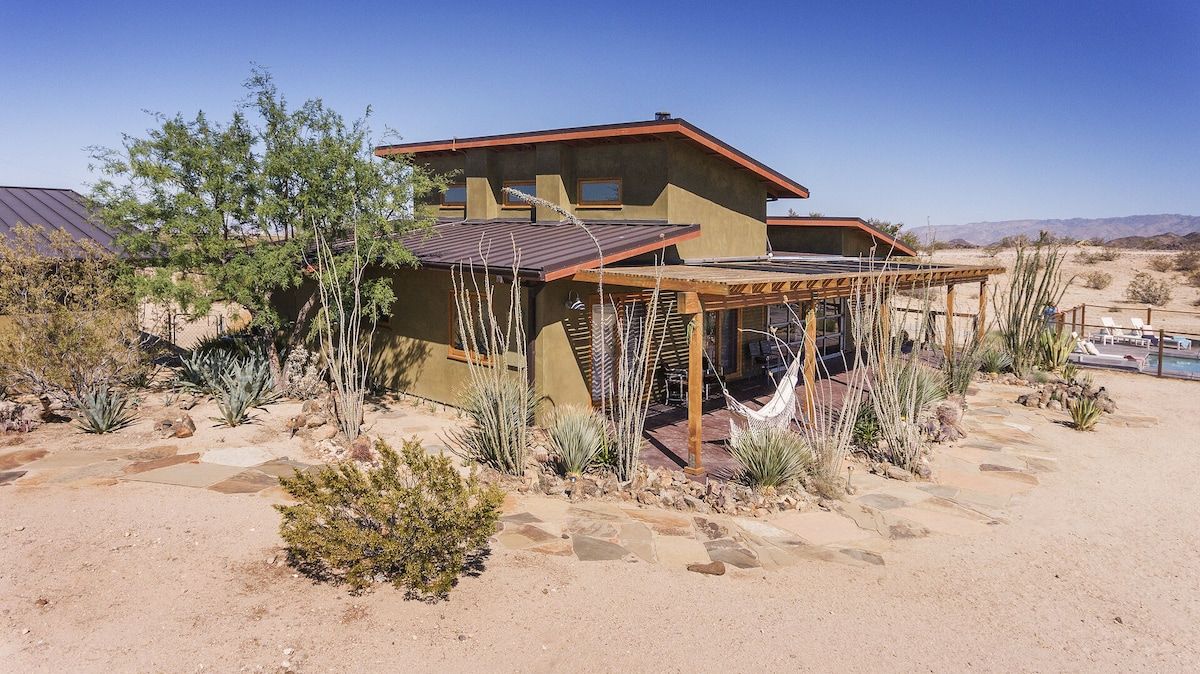 A desert-style house with a patio area, surrounded by cacti and desert plants.
