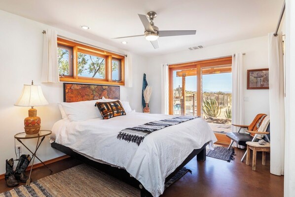 Ein Schlafzimmer mit einem Bett, einem Deckenventilator, einem Fenster und Blick ins Freie.