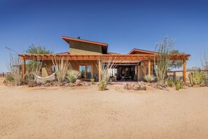 A modern house with a flat roof, wooden pergola, and a desert garden with cacti.