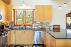 A modern kitchen with wooden cabinets, a built-in oven, a dishwasher, and a large window providing natural light.