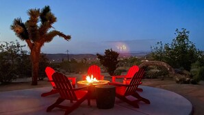 A fire pit with red Adirondack chairs and a view of a desert landscape at dusk. - 🌵 Horizon House | Hot Tub, Fire Pit, Games & BBQ | Adobe in JT 🌵 (Joshua Tree)