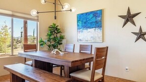 A dining area with a wooden table and chairs, a bench, a potted plant, and a painting on the wall. - Horizon House | Hot Tub, Fire Pit & BBQ in JT (Joshua Tree)