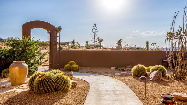A desert landscape with a pathway leading to a gate, surrounded by cacti and a large vase. - 🌵 Horizon House | Hot Tub, Fire Pit, Games & BBQ | Adobe in JT 🌵 (Joshua Tree)
