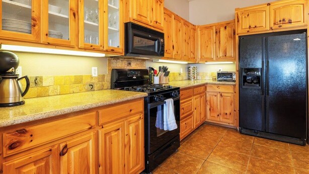 A kitchen with wooden cabinets, a black refrigerator, a stove, and a microwave. - Horizon House | Hot Tub, Fire Pit & BBQ in JT (Joshua Tree)