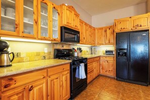 A kitchen with wooden cabinets, a black refrigerator, a stove, and a microwave. - Horizon House | Hot Tub, Fire Pit & BBQ in JT (Joshua Tree)