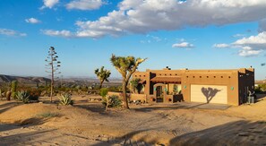 A desert-style building with a garage, surrounded by cacti and a clear sky. - Horizon House | Hot Tub, Fire Pit & BBQ in JT (Joshua Tree)