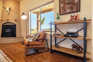 Un salon avec une cheminée, un fauteuil en cuir, une bibliothèque et une grande fenêtre donnant sur un beau paysage.