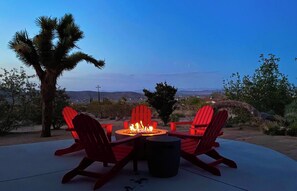 A fire pit with red chairs and a view of the desert landscape. - Horizon House | Hot Tub, Fire Pit & BBQ in JT (Joshua Tree)