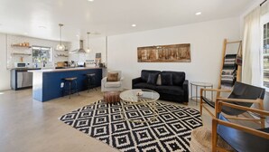 A modern kitchen with a central island, a dining area with a black sofa, and a living room with a patterned rug. - Cosmic Rabbit - Family Friendly home w/Hot Tub (Joshua Tree)