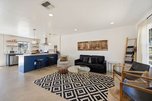A modern kitchen with a central island, a dining area with a black sofa, and a living room with a patterned rug. - Cosmic Rabbit - Family Friendly home w/Hot Tub (Joshua Tree)