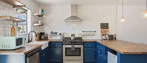 Une cuisine dotée d’une cuisinière en acier inoxydable, de meubles bleus, d’un dosseret de carrelage blanc et d’un plan de travail en bois.