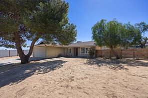 A single-story house with a garage, surrounded by a sandy yard and two trees. - Cosmic Rabbit - Family Friendly home w/Hot Tub (Joshua Tree)