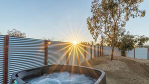 A hot tub with a view of the sunset over a body of water, surrounded by a metal fence and a tree. - Cosmic Rabbit - Family friendly home w/Hot Tub (Joshua Tree)