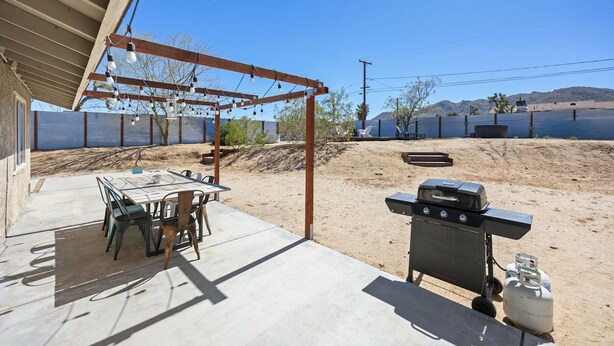 An outdoor patio with a table and chairs, a barbecue grill, and a pergola with string lights. - Cosmic Rabbit - Family Friendly home w/Hot Tub (Joshua Tree)