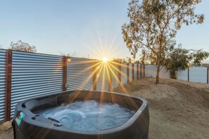 A hot tub with a sunset in the background, surrounded by a metal fence and a tree. - Cosmic Rabbit - Family Friendly home w/Hot Tub (Joshua Tree)