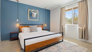 A bedroom with a bed, nightstands, a wall-mounted light fixture, a framed cow head decoration, and a large window with curtains. - Cosmic Rabbit - Family friendly home w/Hot Tub (Joshua Tree)