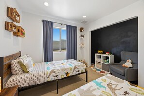 A child's bedroom with a bed, a chair, a shelf with toys, and a window with curtains. - Cosmic Rabbit - Family Friendly home w/Hot Tub (Joshua Tree)