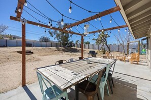 An outdoor patio with a wooden table and chairs, string lights, and a barbecue grill.