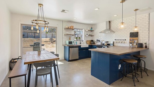 A modern kitchen with a central island, bar stools, and a dining area with a table and chairs. - Cosmic Rabbit - Family friendly home w/Hot Tub (Joshua Tree)