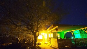 Una casa con porche y un árbol frente, bajo un cielo nocturno estrellado.