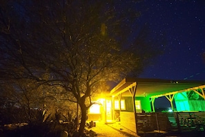 Una casa amb un porxo i un arbre al davant, sota un cel estrellat.