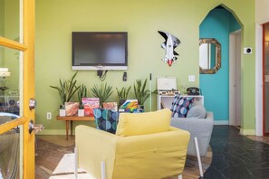 Una sala de estar con televisor de pantalla plana, dos sofás, una mesa de centro y varias plantas en macetas.