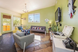 Un salon comprenant un canapé, un fauteuil et une table basse. Un téléviseur est fixé au mur, ainsi qu’un téléphone et un objet décoratif qui ressemble à un vaisseau spatial.