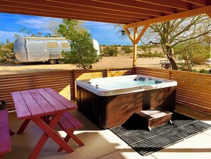 Un patio exterior con un jacuzzi, una mesa de picnic y una caravana al fondo.