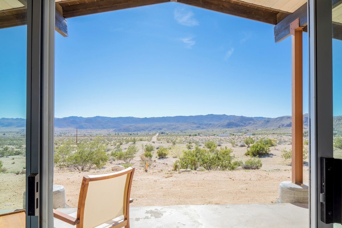Una habitación con un amplio ventanal que da a un paisaje desértico con montañas al fondo.