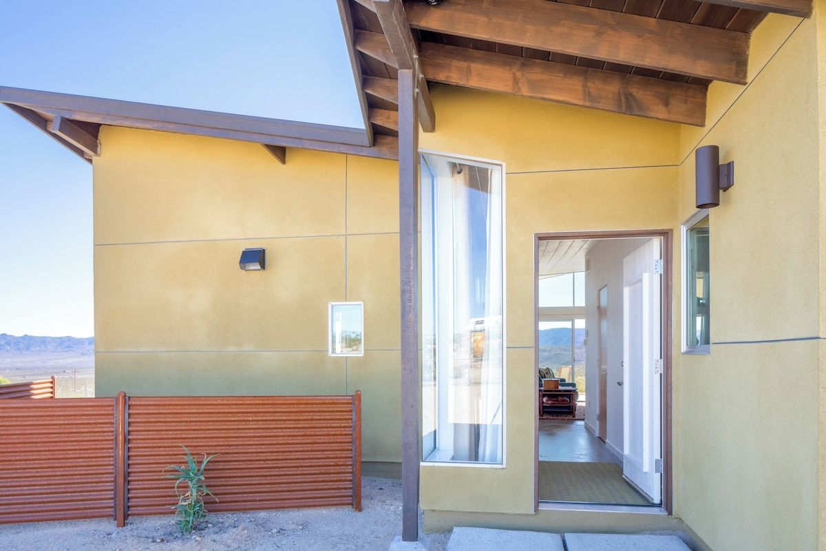 A modern building with a yellow facade, large windows, and a wooden bench.