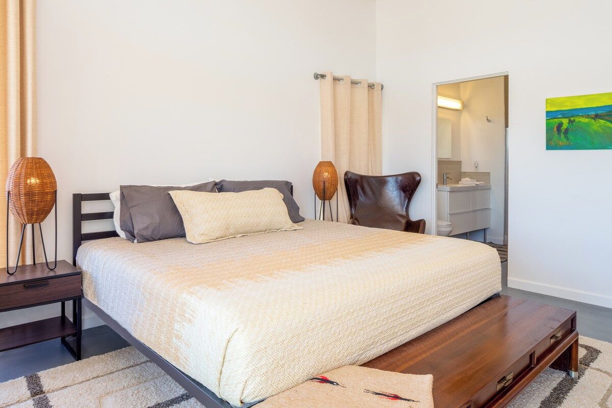 A bedroom with a bed, bedside tables, a mirror, and a painting on the wall.