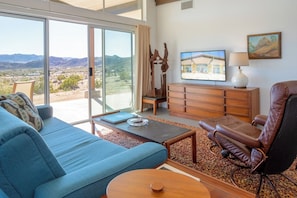 A living room with a blue sofa, a leather recliner, a wooden coffee table, and a view of the desert through large sliding glass doors.