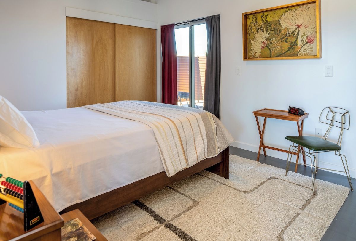 Une chambre à coucher avec un lit, un bureau, une chaise, une horloge et un tableau accroché au mur.