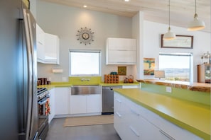 A modern kitchen with white cabinets, a green countertop, and a stainless steel refrigerator.