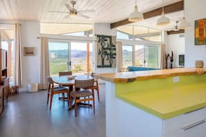 A modern kitchen with a dining area, large windows, and a view of the mountains.