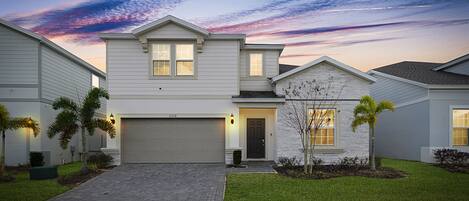 A two-story house with a garage, a small front yard with a tree, and a driveway leading to the garage.