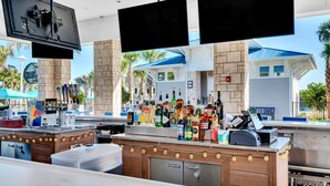 A bar area with a counter, multiple liquor bottles, a cash register, and two TVs mounted above the bar. - Newly Renovated 8BR Villa with Heated Pool & Spa | Minutes from Disney (Davenport)