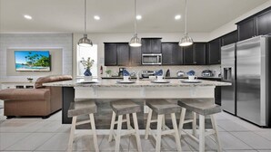 A modern kitchen with dark cabinets, a large island with bar stools, stainless steel appliances, and pendant lighting. - Newly Renovated 8BR Villa with Heated Pool & Spa | Minutes from Disney (Davenport)