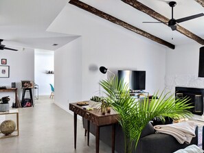 A modern living room with a fireplace, a television, and a dining area with a table and chairs. - Campero House: Meditation Room & Near Joshua Tree (Yucca Valley)
