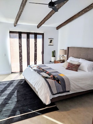A bedroom with a bed, a ceiling fan, a nightstand, a lamp, a cactus, and a sliding glass door. - Campero House: Meditation Room & Near Joshua Tree (Yucca Valley)