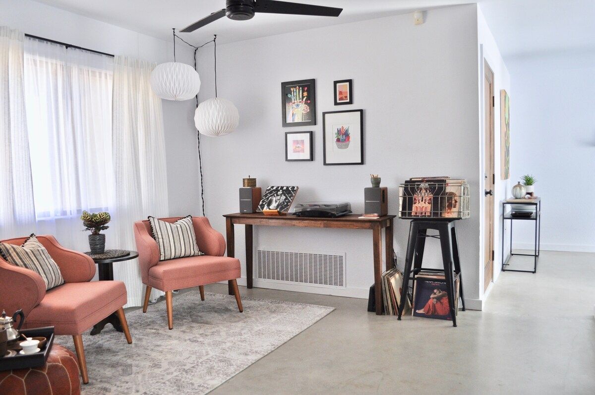 A modern living room with two sofas, a coffee table, a side table, a standing fan, and a bookshelf.