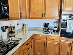 A kitchen with wooden cabinets, a gas stove, a microwave, a coffee maker, and a blender.