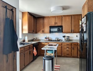 A kitchen with wooden cabinets, a black refrigerator, a microwave, and a stainless steel sink. - Campero House: Meditation Room & Near Joshua Tree (Yucca Valley)