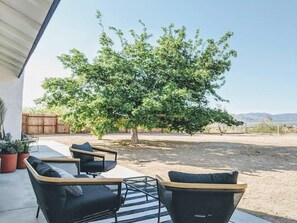 An outdoor seating area with two chairs and a table, a tree, and a clear sky. - Campero House: Meditation Room & Near Joshua Tree (Yucca Valley)