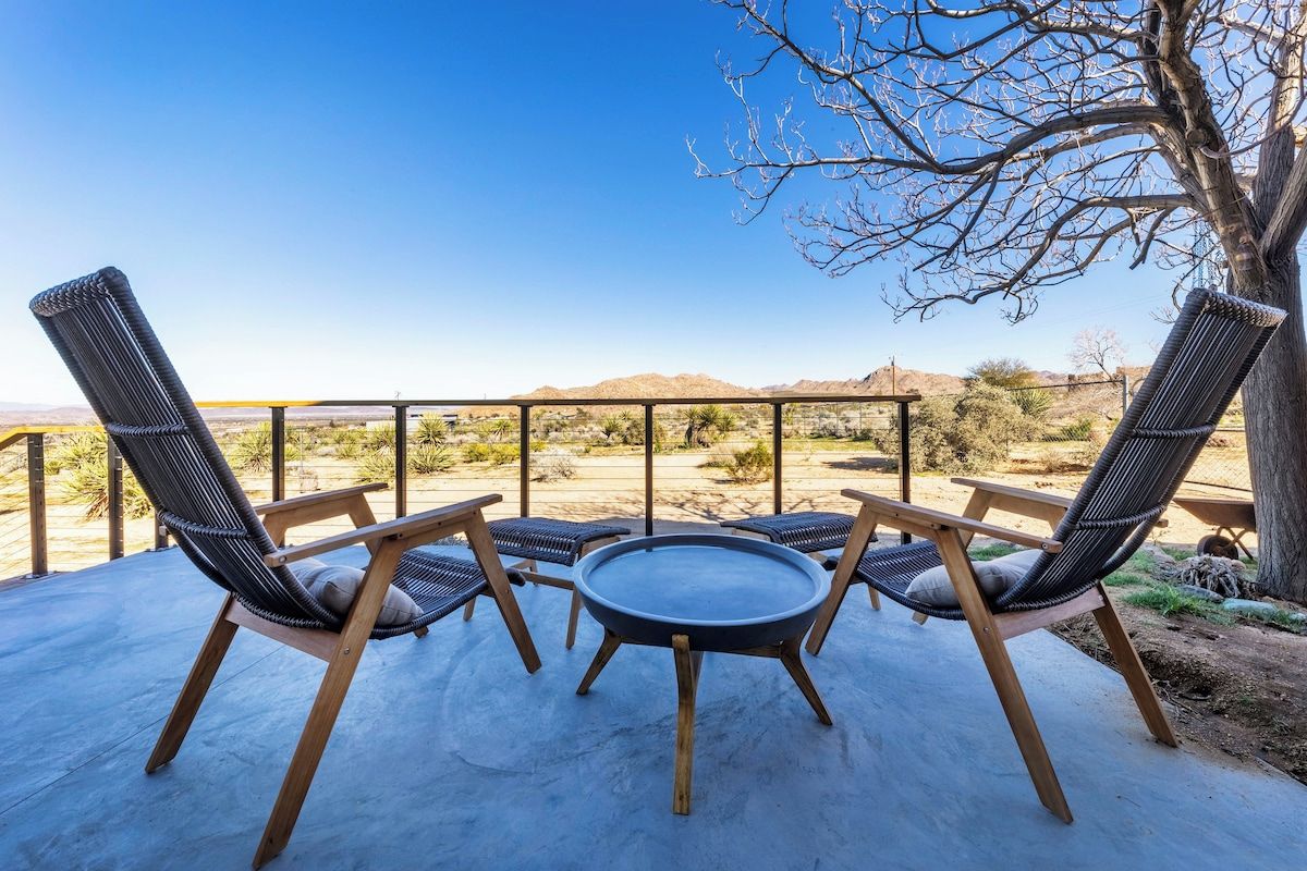 A patio with three wicker chairs and a round table, overlooking a desert landscape.