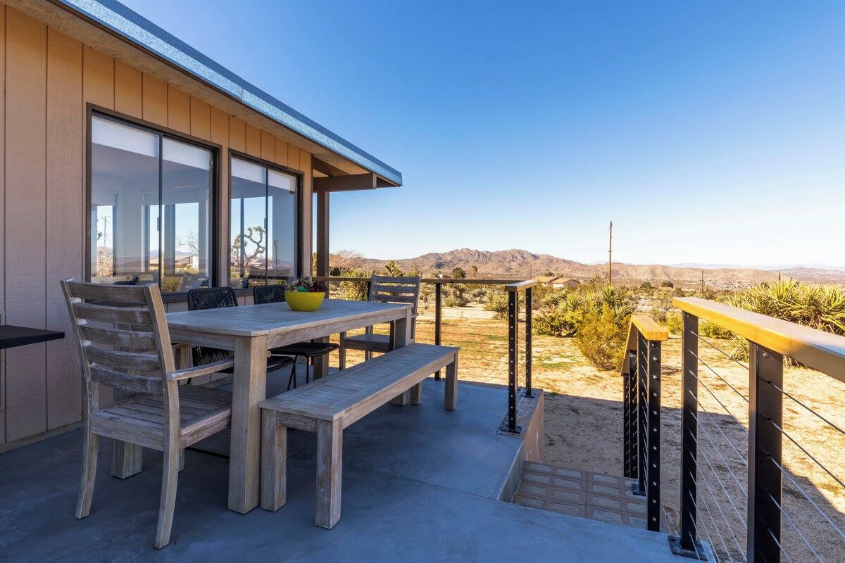 An outdoor patio with a wooden table and chairs, a bench, and a view of the desert landscape.